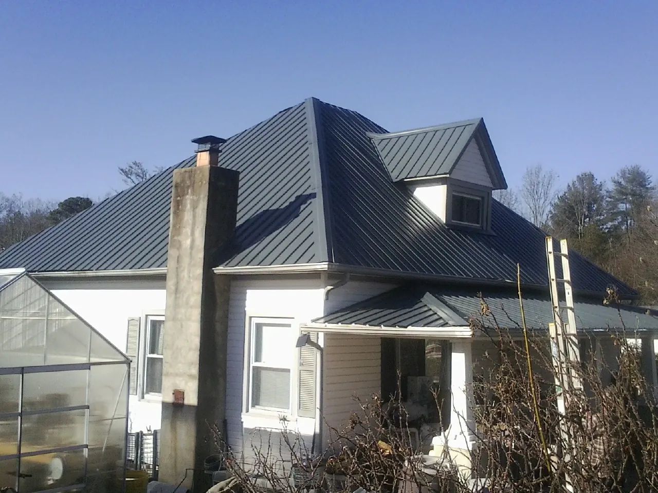 Dark blue standing seam metal roof on a white farmhouse with dormer — Slate & Tile Roof Repair by Roofing Brothers in Westlake Village