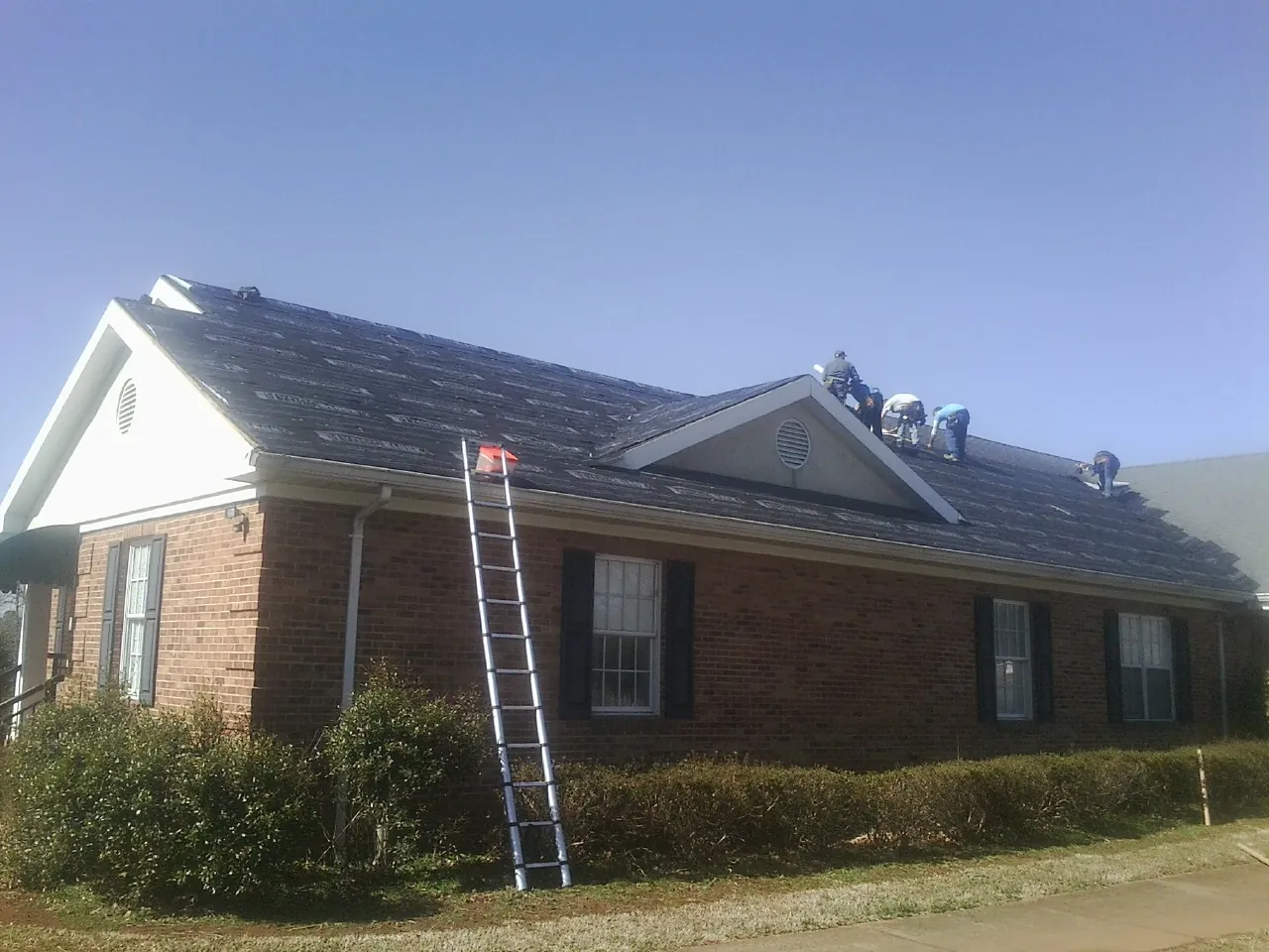 Crew tearing shingles off a brick ranch roof with a ladder set — Emergency Roof Repair work by our crew in Westlake Village