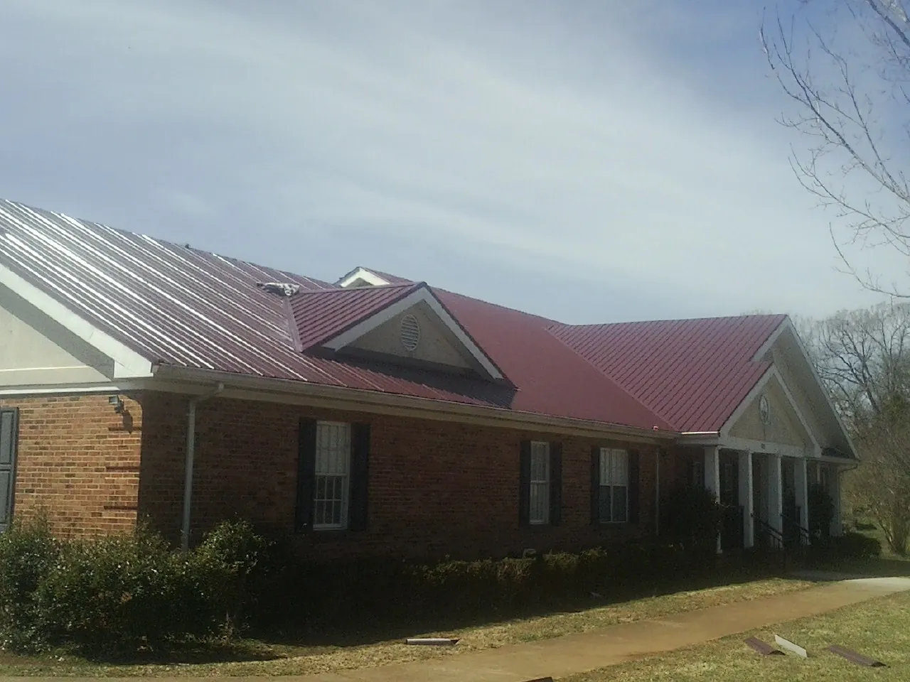 Red metal roof with gabled entries on a long brick building, from a Hail Damage Roof Repair job in Westlake Village