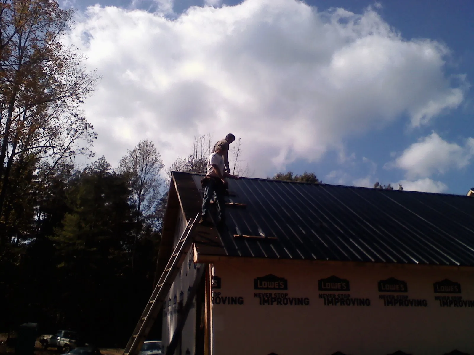 Roofer fastening dark metal panels high against a cloudy sky, from a Roof Inspection job in Westlake Village