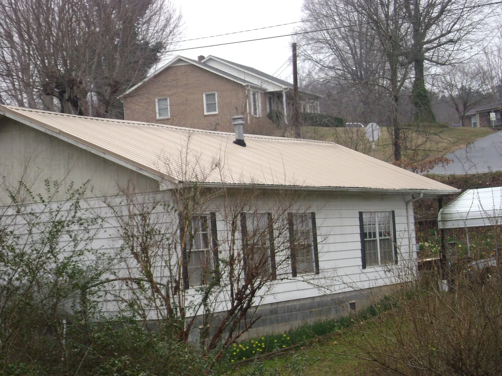 Tan metal roof on a white sided house set into a hillside — Commercial Roofing by Roofing Brothers in Westlake Village